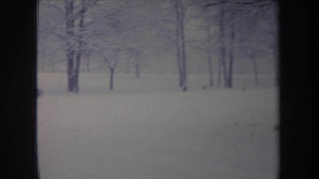 1968 Michigan home-movie frame showing a snow-covered yard, bare trees, and an older car partly visible in the distance.
