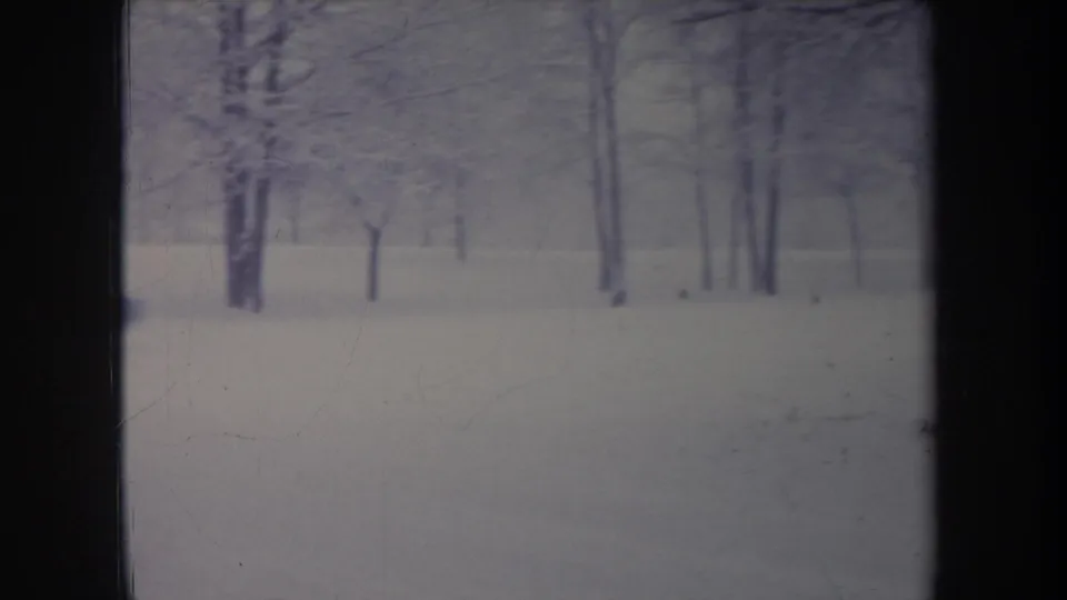 1968 Michigan home-movie frame showing a snow-covered yard, bare trees, and an older car partly visible in the distance.