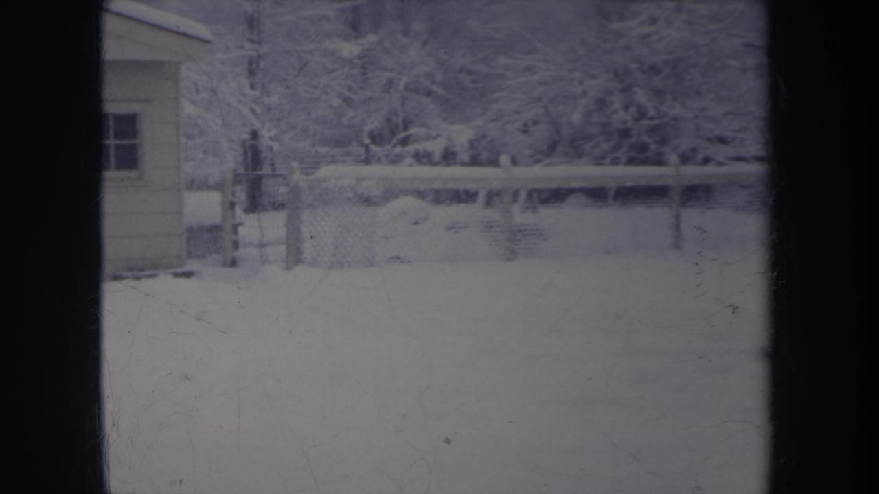 1968 Michigan 8mm frame showing a snow-covered yard, chain-link fence, small shed, and dense winter trees.