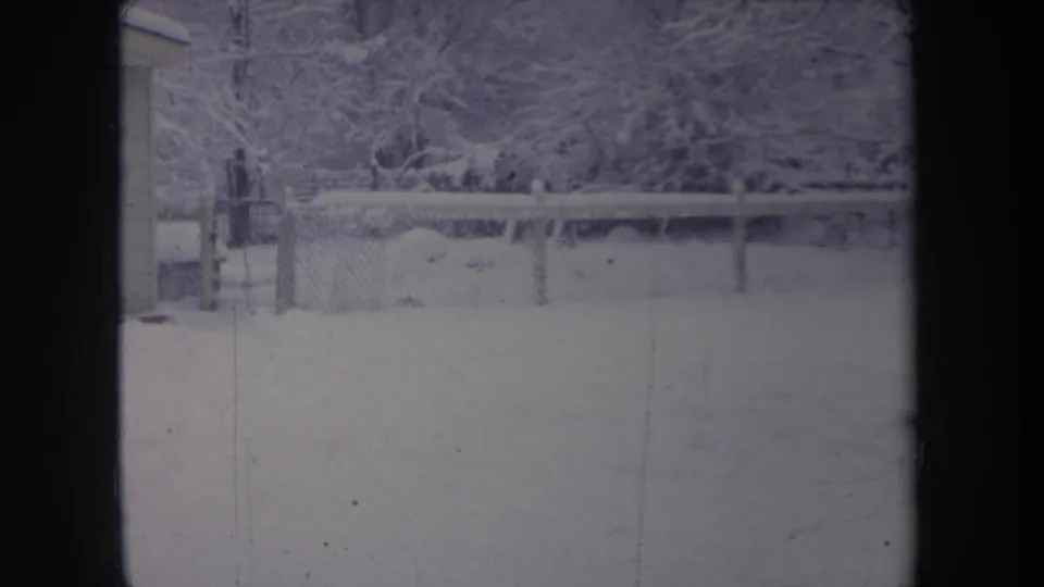 1968 Michigan winter frame with a chain-link fence, snow-covered yard, trees, and the edge of a small shed.