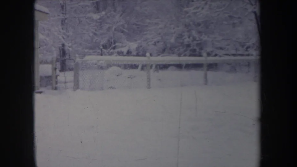 1968 Michigan 8mm frame showing a snow-covered yard, chain-link fence, and bare trees viewed through a dark window frame.