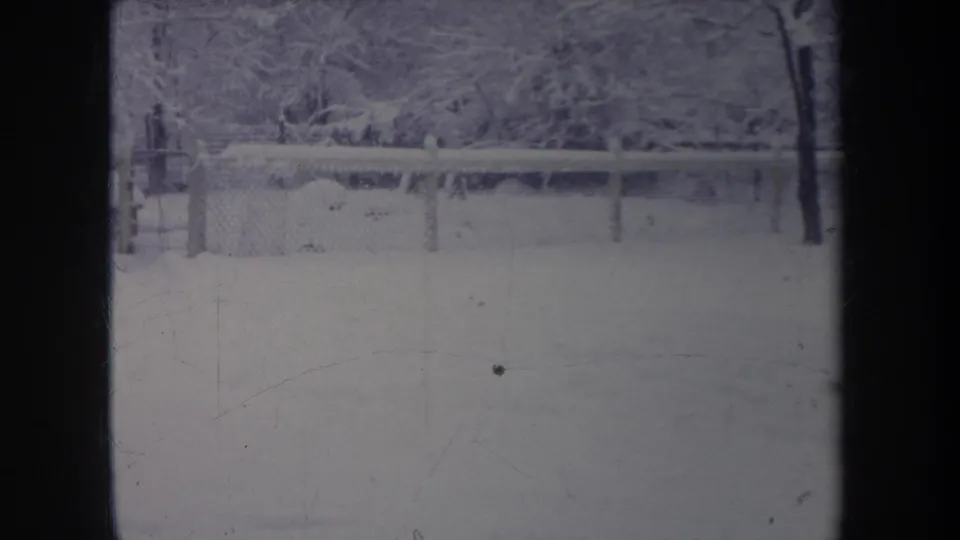 1968 Michigan 8mm frame of a snow-filled backyard and fence, softened by grain, scratches, and contact-sheet overlap.