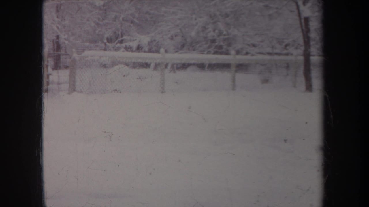 1968 Michigan 8mm frame showing a snow-covered yard, fence line, and winter trees in soft faded color.