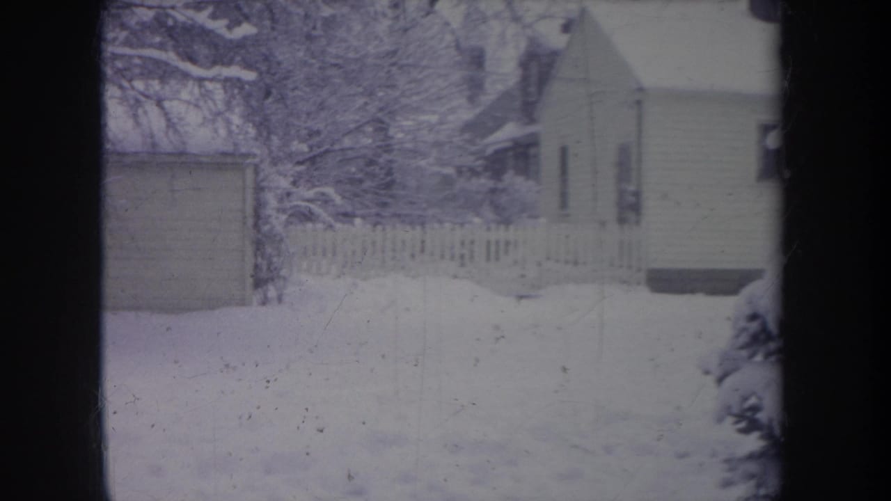 1968 Michigan 8mm frame showing a snowy residential yard, picket fence, shed edge, trees, and part of a modest house.