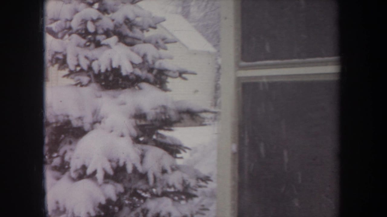 1968 Michigan 8mm frame with a close view of thick snow on evergreen branches beside a house window and wall.
