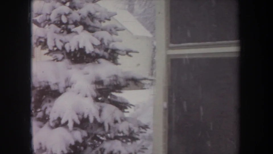 1968 Michigan 8mm frame with a close view of thick snow on evergreen branches beside a house window and wall.