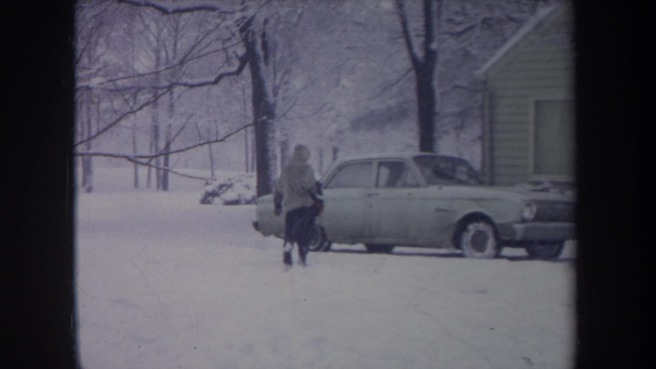 The figure nears the light-colored car beside a house, with bare trees and deep snow visible in the 1968 Michigan frame.