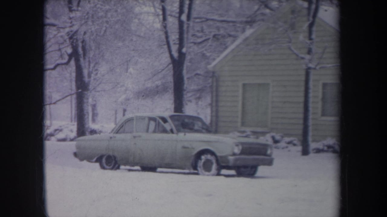 1968 Michigan 8mm frame showing a light-colored sedan stationary in a snowy residential setting after the passenger door is closed or nearly closed.