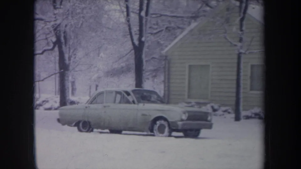 1968 Michigan 8mm frame showing a light-colored sedan stationary in a snowy residential setting after the passenger door is closed or nearly closed.