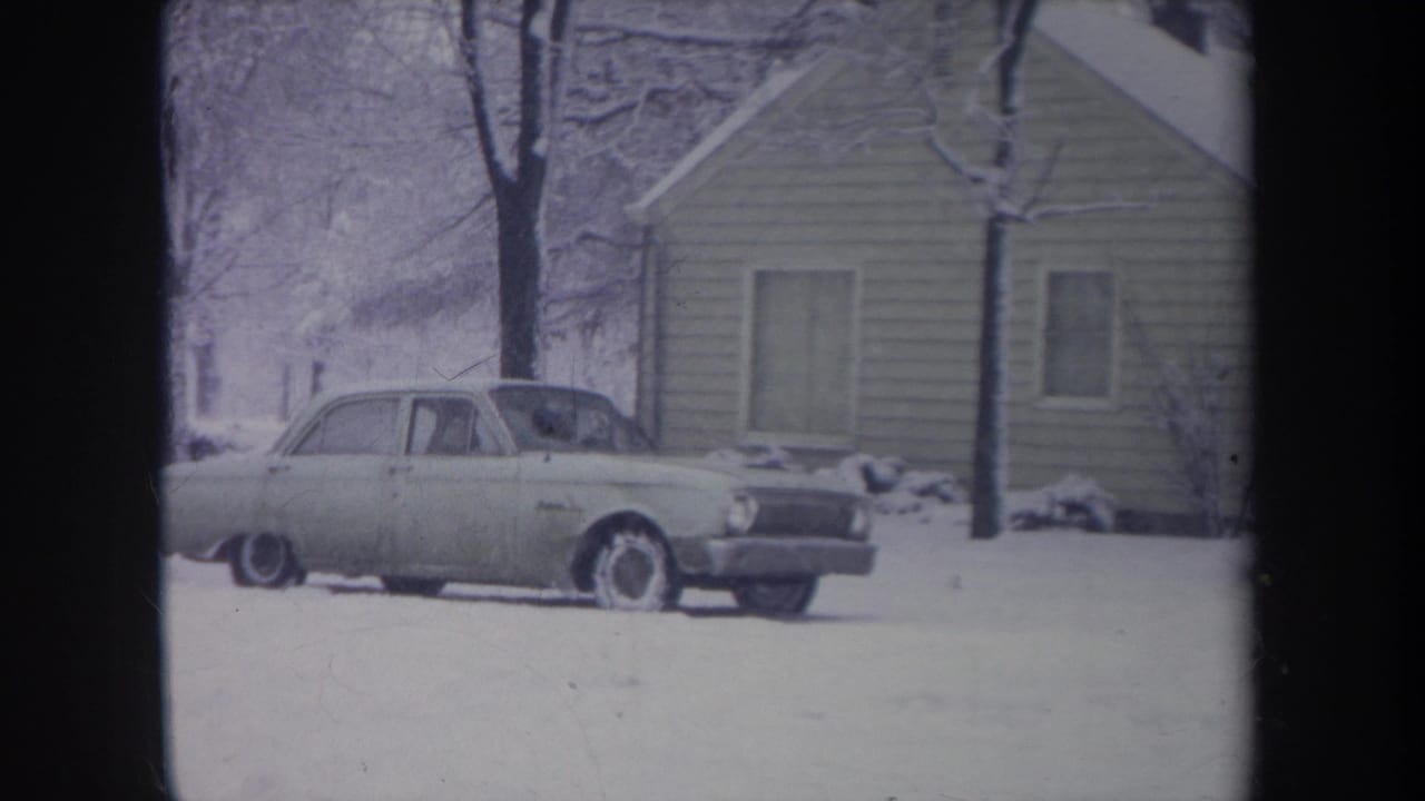 1968 Michigan home-movie frame of a light-colored sedan in a snowy residential yard beside a modest house.