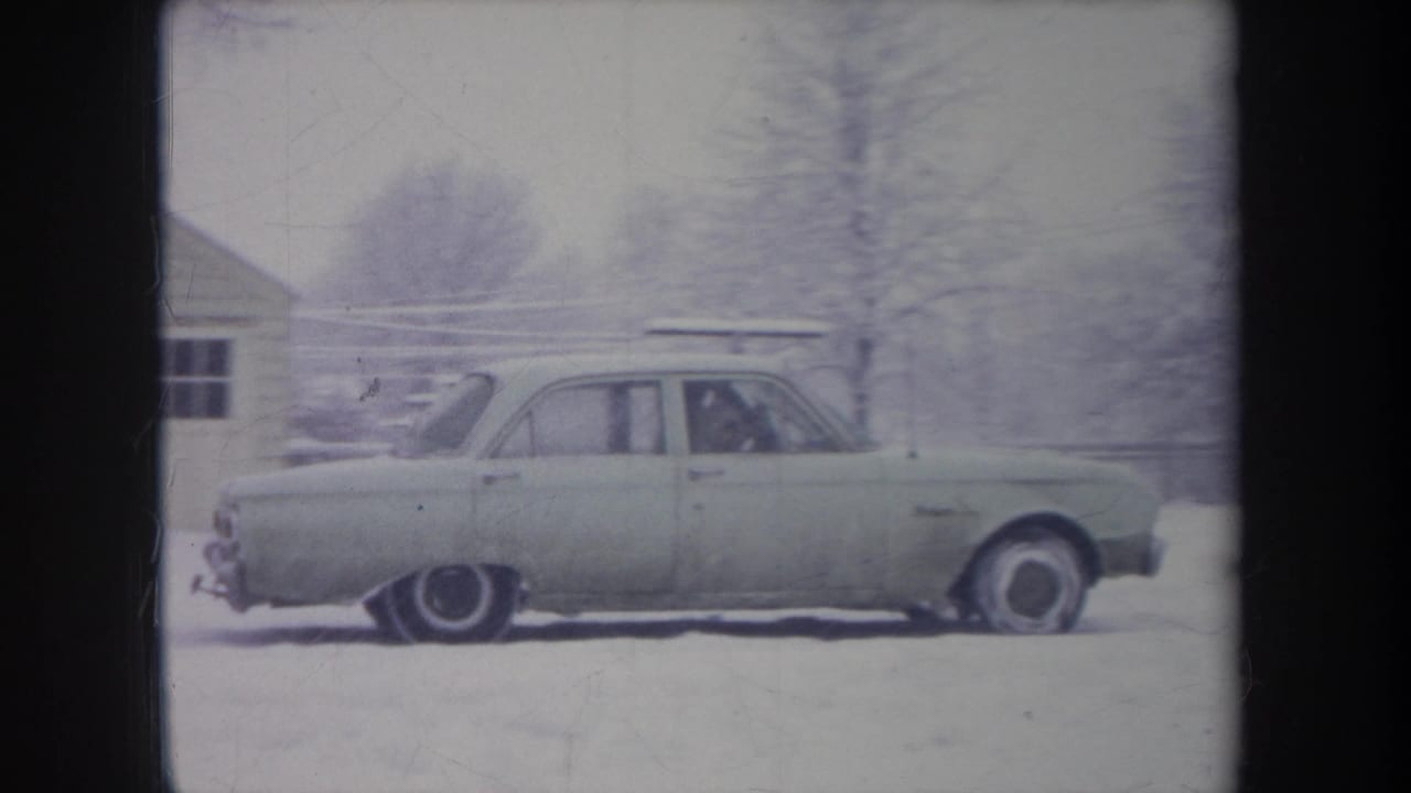 Sedan seen in profile on snowy ground with a driver visible inside.