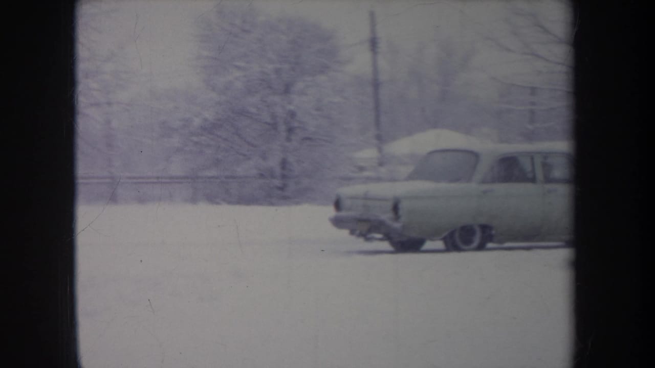The light-colored sedan moves through snow in a residential Michigan setting, partly framed by winter trees.