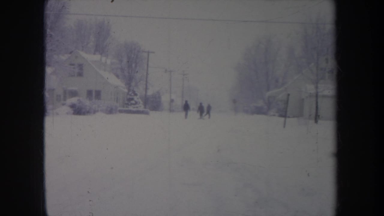 Distant figures stand or walk on a snow-covered Michigan residential street in this 1968 metadata-supported 8mm frame.