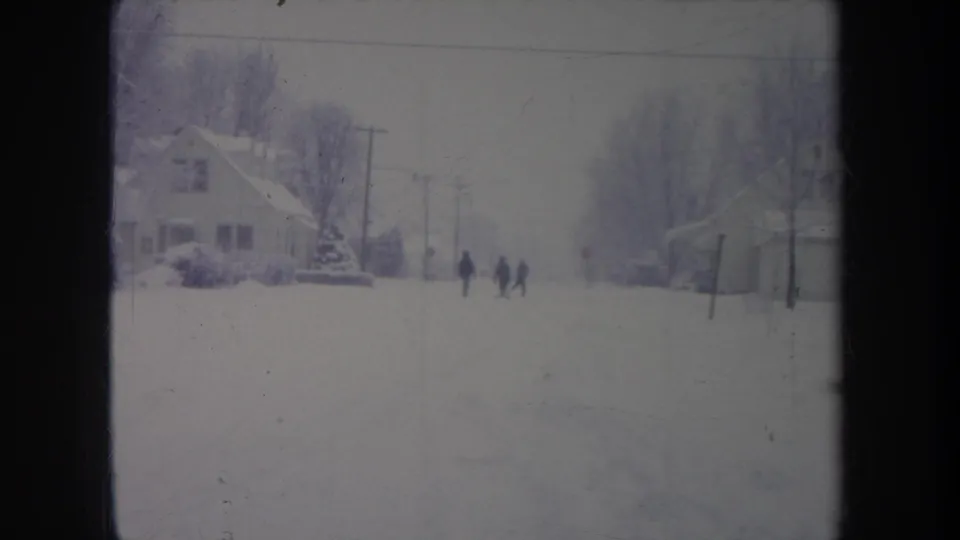 Distant figures stand or walk on a snow-covered Michigan residential street in this 1968 metadata-supported 8mm frame.