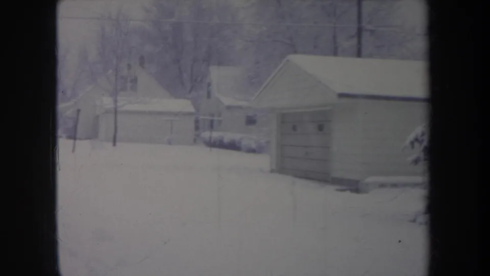 1968 Michigan 8mm frame with snowy garages, low houses, bare trees, and an overcast residential backdrop.