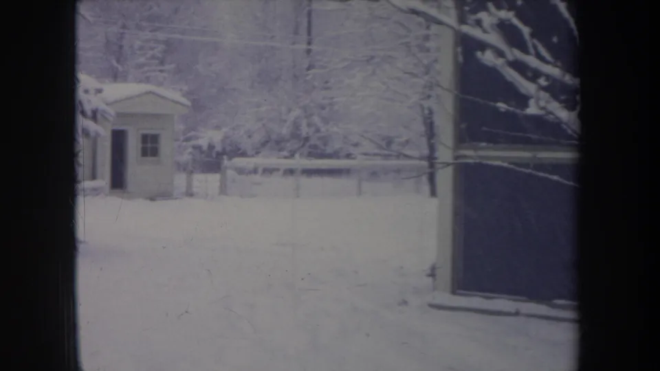 1968 Michigan 8mm frame of a snowy residential yard, small shed, fence, bare trees, and a dark window or doorway edge.