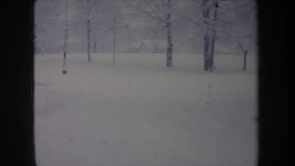 1968 Michigan winter landscape on 8mm, with flat snow cover, distant bare trees, and visible gate shadowing at the frame edges.