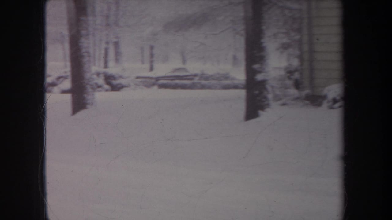1968 Michigan 8mm frame showing a snow-covered yard or wooded edge with bare trees, low branches, and a possible structure edge.