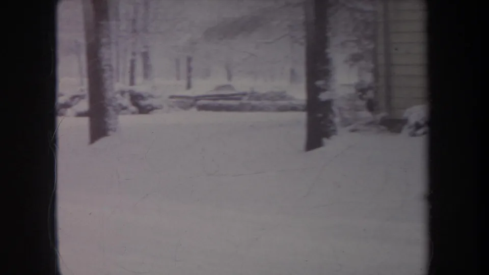 1968 Michigan 8mm frame showing a snow-covered yard or wooded edge with bare trees, low branches, and a possible structure edge.