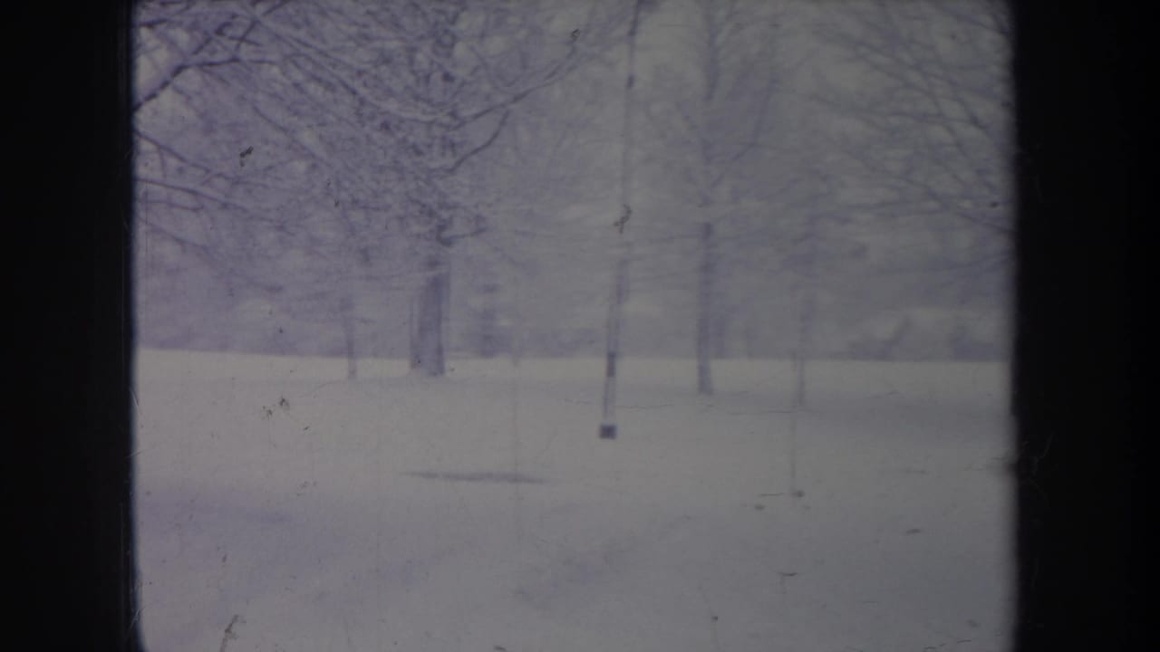 Faded 1968 Michigan 8mm frame showing snowy ground, leafless trees, a slender pole, and soft winter haze.