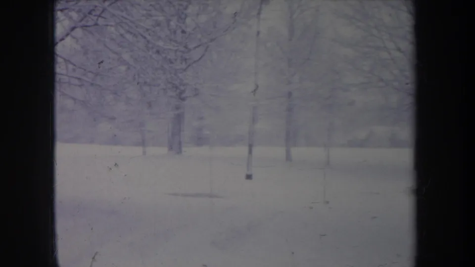 Faded 1968 Michigan 8mm frame showing snowy ground, leafless trees, a slender pole, and soft winter haze.