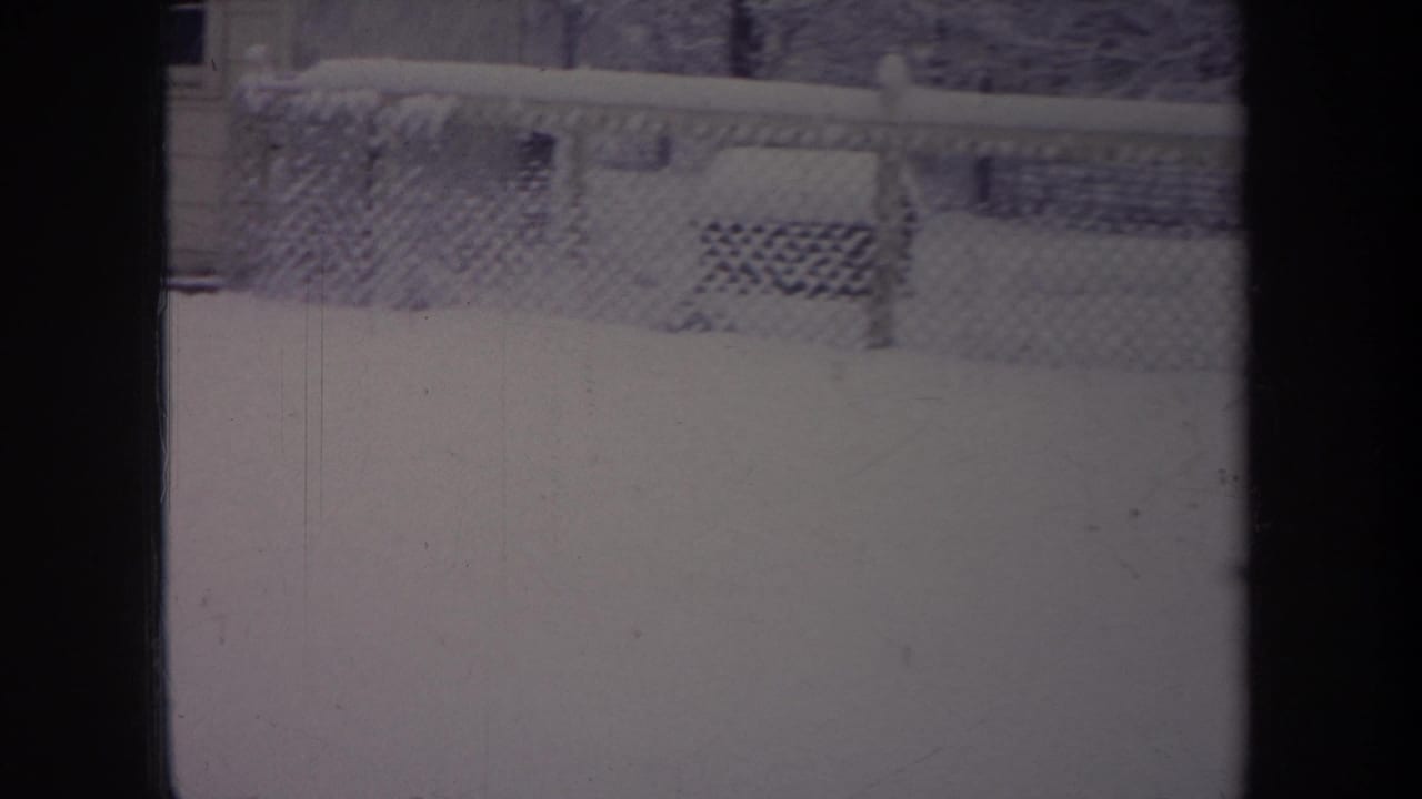 1968 Michigan 8mm frame showing a snow-covered yard through a dark window frame, with a chain-link fence across the background.