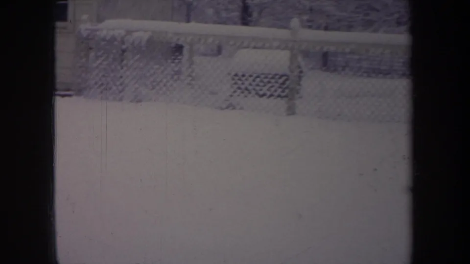 1968 Michigan 8mm frame showing a snow-covered yard through a dark window frame, with a chain-link fence across the background.