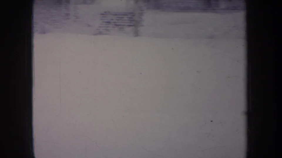 Soft 8mm frame of a Michigan snowy backyard with chain-link fencing and dark foreground bars.