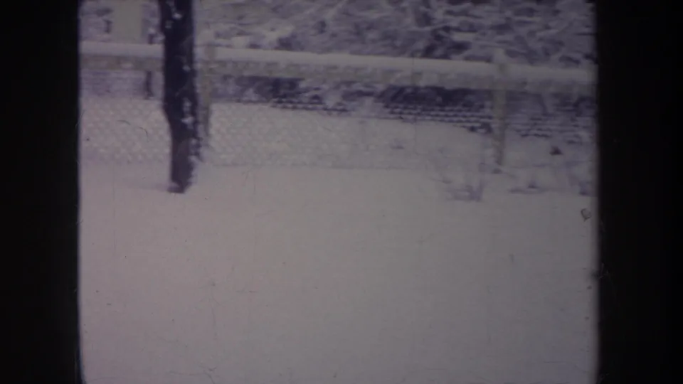 1968 Michigan 8mm frame showing a snow-covered yard, chain-link fence, and bare winter trees, partly obscured by dark vertical bars.