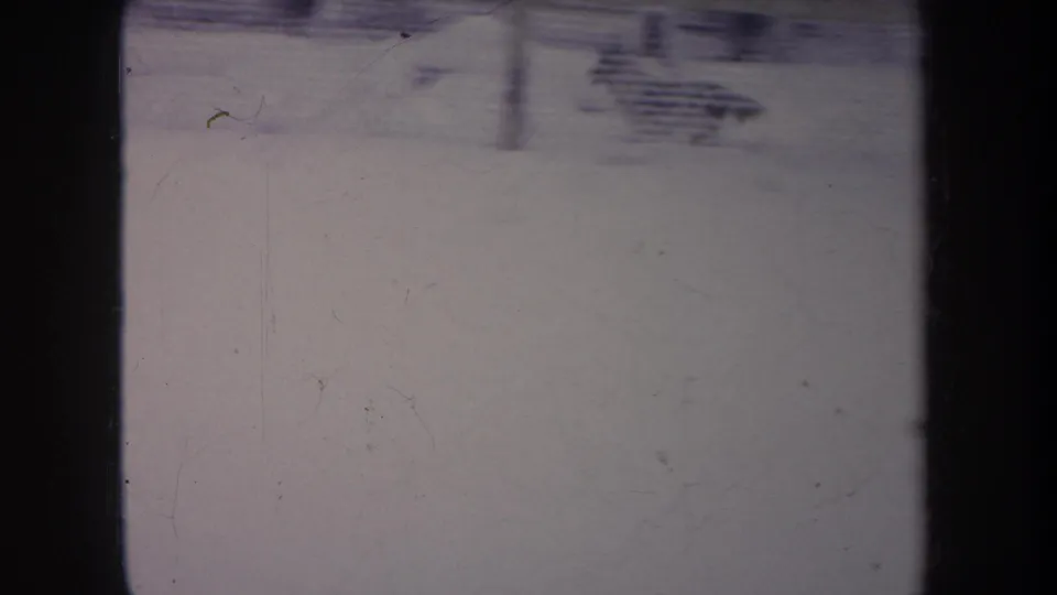 1968 Michigan 8mm frame with a blurred small dark figure crossing the snow near a fence, captured with motion smear and grain.