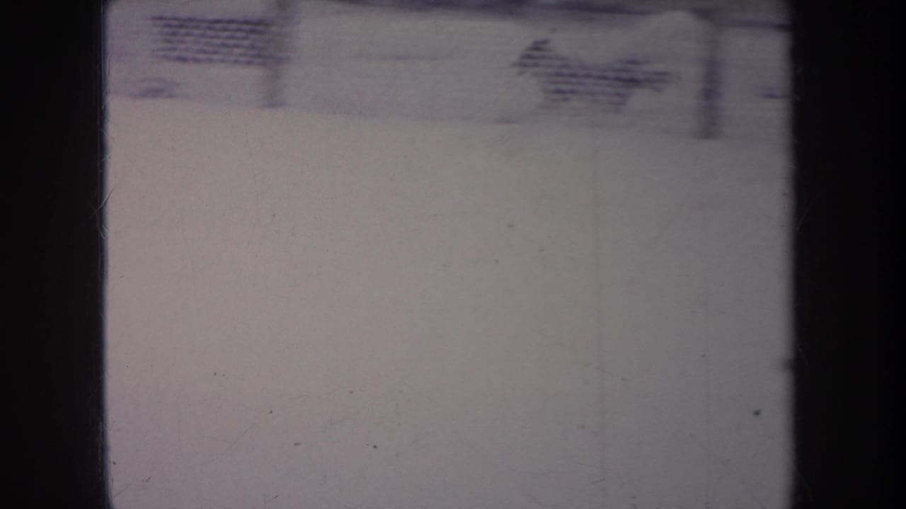 1968 Michigan 8mm frame showing a snowy outdoor area and chain-link fence, with heavy gate edges and soft archival exposure.