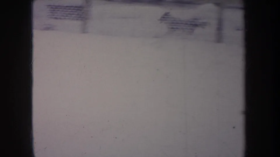 1968 Michigan 8mm frame showing a snowy outdoor area and chain-link fence, with heavy gate edges and soft archival exposure.