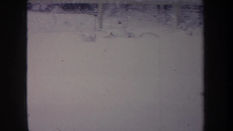 1968 Michigan 8mm frame showing a snowy fenced outdoor area with faint dark animal forms and strong archival film texture.