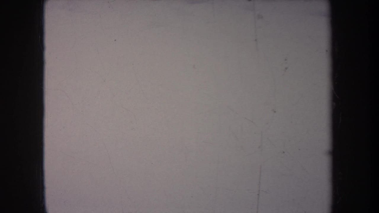 Pale scratched frame with dark 8mm borders and only faint outdoor detail visible.