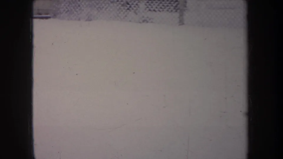 Snowy Michigan backyard view on 8mm film, with a chain-link fence and dark frame edges visible beneath scratches.