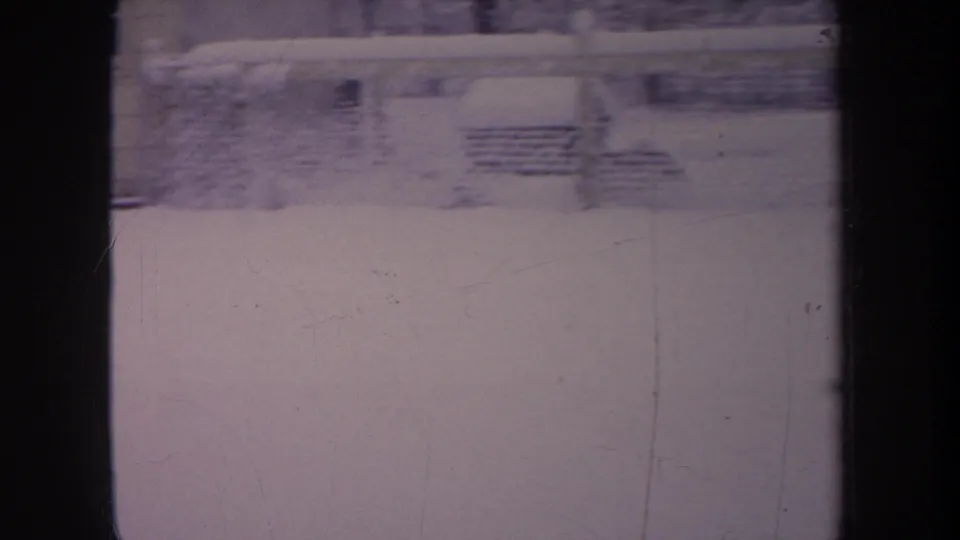 1968 Michigan 8mm still with a small dark dog crossing deep snow near a chain-link fence in a backyard.