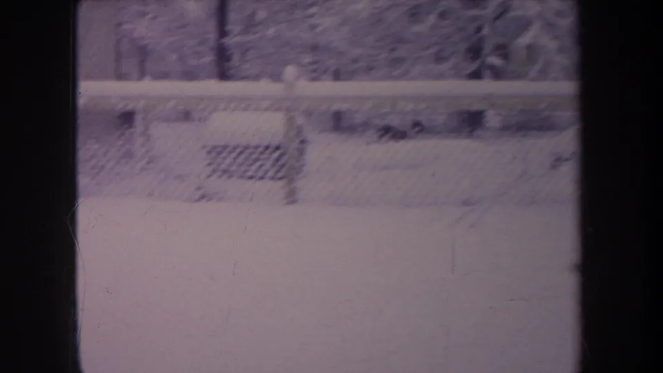 1968 Michigan 8mm frame showing a purple-tinted snowy backyard with chain-link fence, trees, and dark film-frame edges.