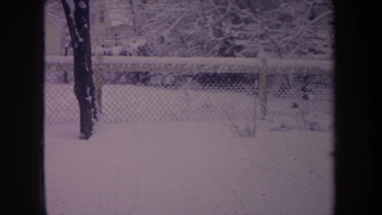 1968 Michigan home-movie frame showing a snow-covered backyard, fence, trees, and dark framing from the camera view.