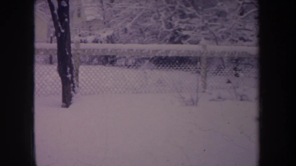 1968 Michigan home-movie frame showing a snow-covered backyard, fence, trees, and dark framing from the camera view.