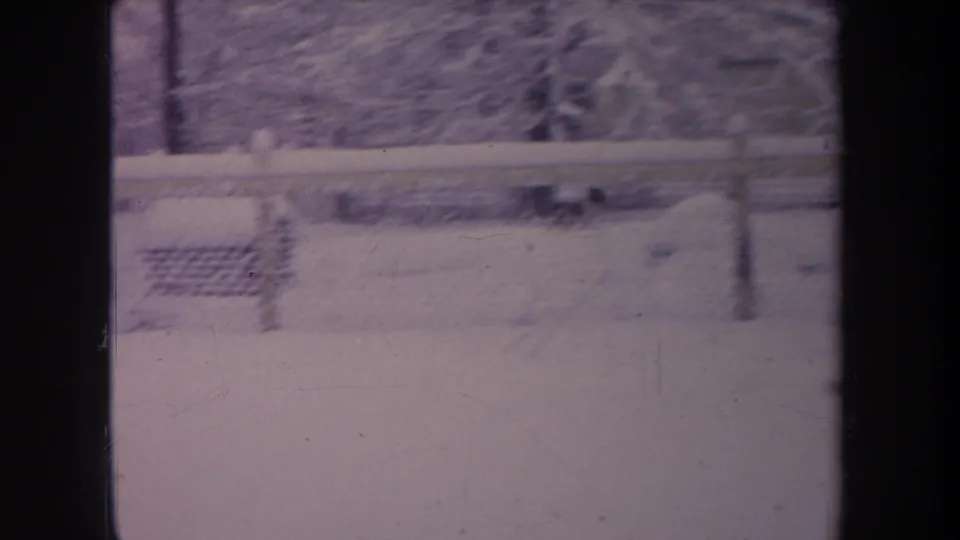 1968 Michigan 8mm frame showing a snowy yard or roadside with chain-link fence, bare trees, and dark window mullions in the foreground.