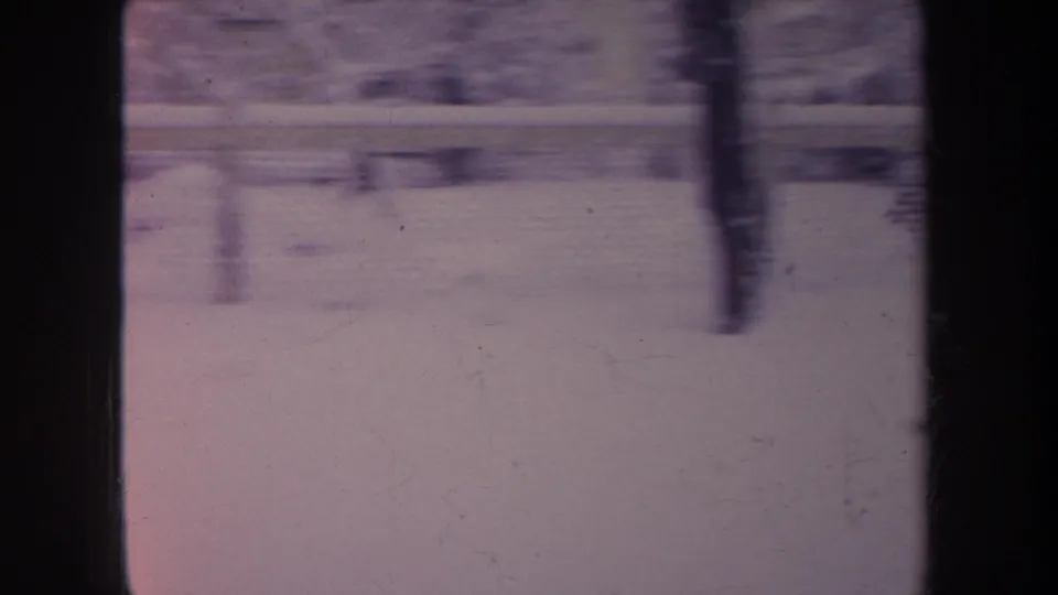 1968 Michigan 8mm frame with a soft, slightly blurred view of snow, chain-link fencing, and winter trees through window framing.