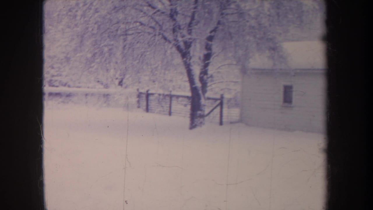 1968 Michigan 8mm frame showing a snow-covered yard, small garage, bare tree, and wooden fence in soft winter light.
