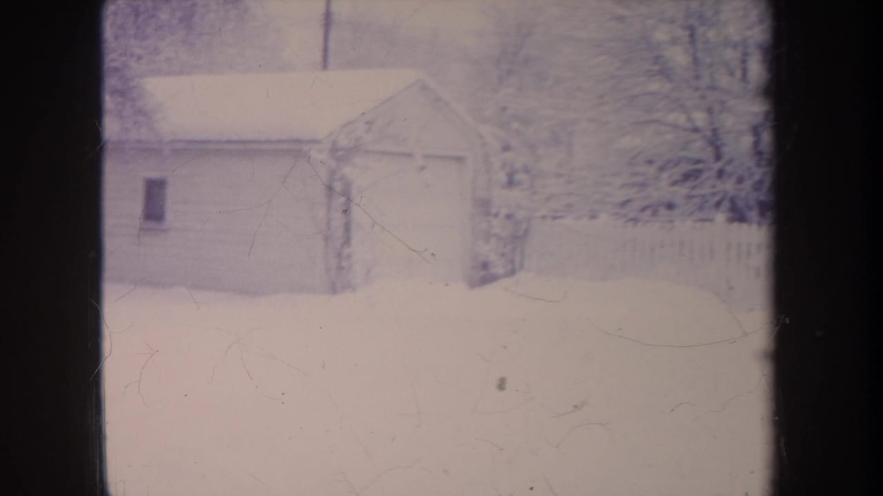 1968 Michigan 8mm frame with a small garage, snowy yard, bare trees, and fence, partly divided by dark framing.