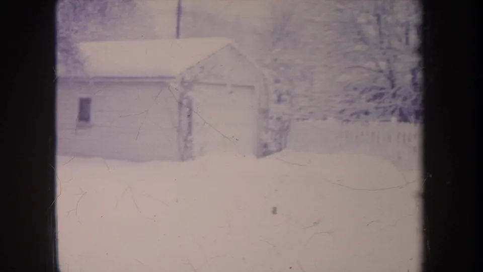 1968 Michigan 8mm frame with a small garage, snowy yard, bare trees, and fence, partly divided by dark framing.