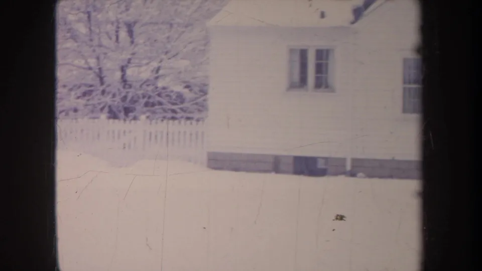 1968 Michigan 8mm frame showing a white clapboard house, snow-covered yard, bare tree, and picket fence.