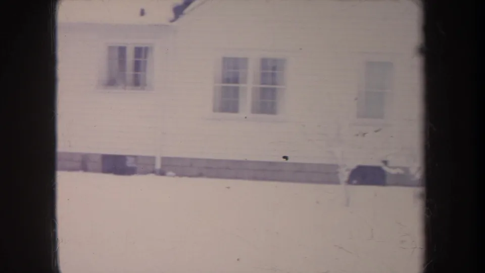 1968 Michigan 8mm frame of a white house exterior with multi-pane windows and deep snow in the foreground.