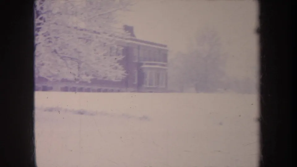 8mm home-movie frame from Michigan showing a snow-covered yard and a partial brick school building during winter.