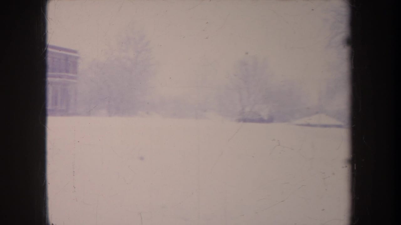 Soft 1968 Michigan winter frame with an open snowfield, distant bare trees, and part of a brick building at the edge.