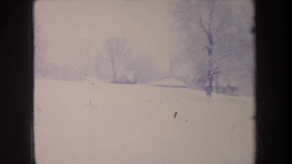 1968 Michigan 8mm frame showing a snow-covered field, leafless trees, and faint distant buildings through pale winter haze.