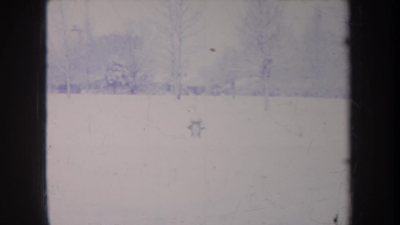 Faded 1968 Michigan 8mm frame showing snow-covered ground, bare trees, and distant structures softened by haze and film texture.